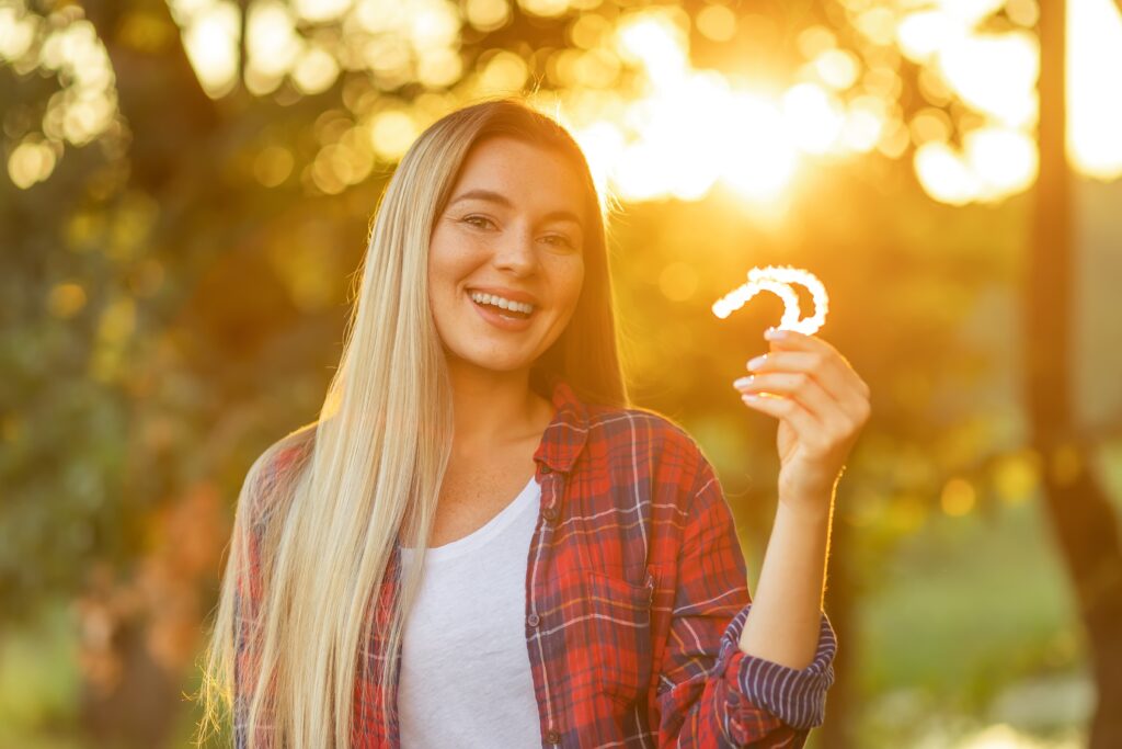 young woman holding up her clear aligners at sun set