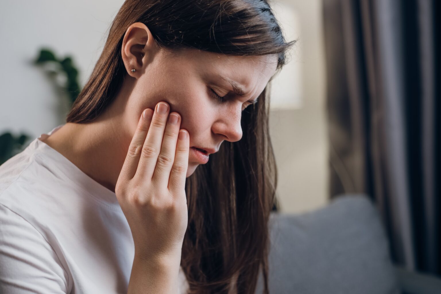 closeup of a young woman suffering from tooth pain, hand on jaw